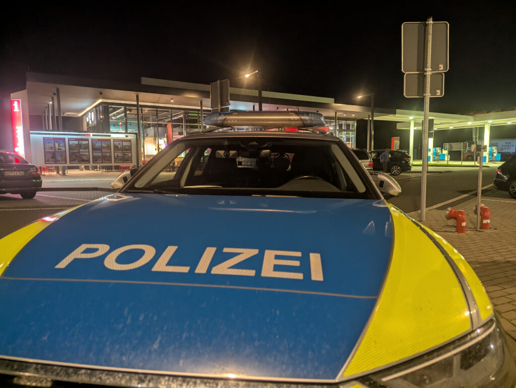 Ein modernes Polizeiauto steht nachts in Kirchworbis, Thüringen. Das Fahrzeug ist geparkt und scheint bereit für den Einsatz zu sein. Im Hintergrund sind beleuchtete Gebäude und ein Schnellrestaurant erkennbar.
